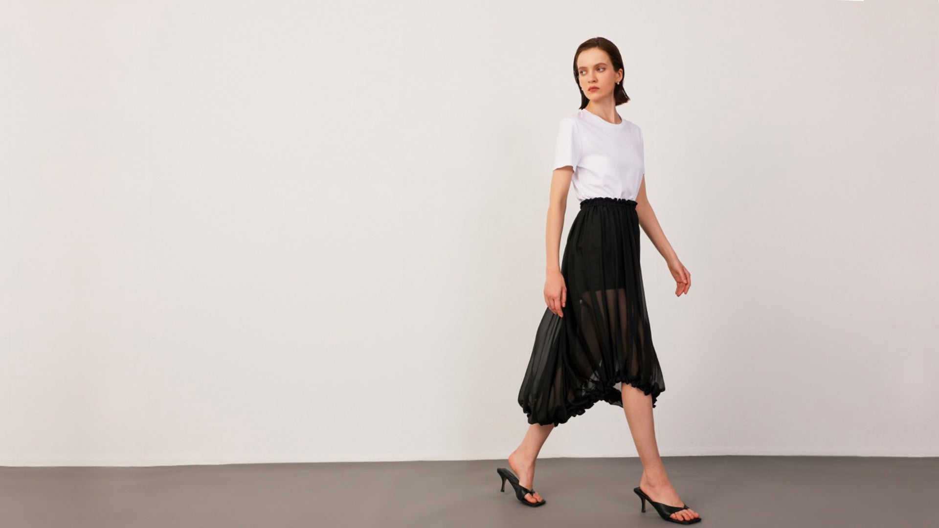 Model wearing Ellie Silk Chiffon Midi-Skirt in Black and Bree Mulberry Silk-Cotton T-Shirt in White, striking a dynamic pose that showcases movement and flow.